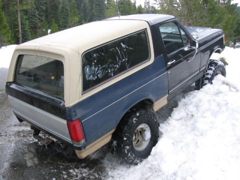 1989 Ford Bronco - A blue and tan Ford Bronco with a white camper shell is stuck in a snowdrift.