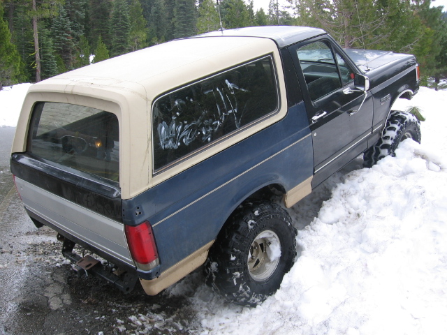 Blue and tan Ford Bronco with a white camper shell stuck in snow