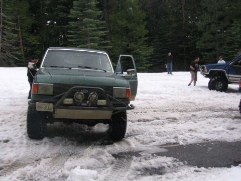 1989 Ford Bronco - A green Ford truck sits in a snowy area with trees in the background and other vehicles nearby.