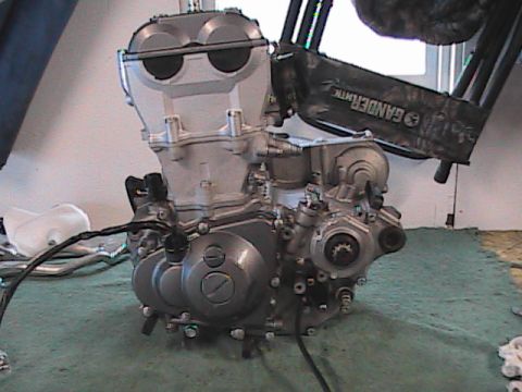 2007 Yamaha YZ450F - A motorcycle engine is shown disassembled and resting on a green mat. Text is visible on a black object in the background.