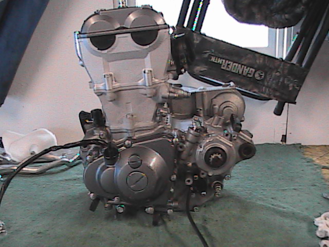 Motorcycle engine on a green mat. Text on a black object reads 'GANDERMATIC'