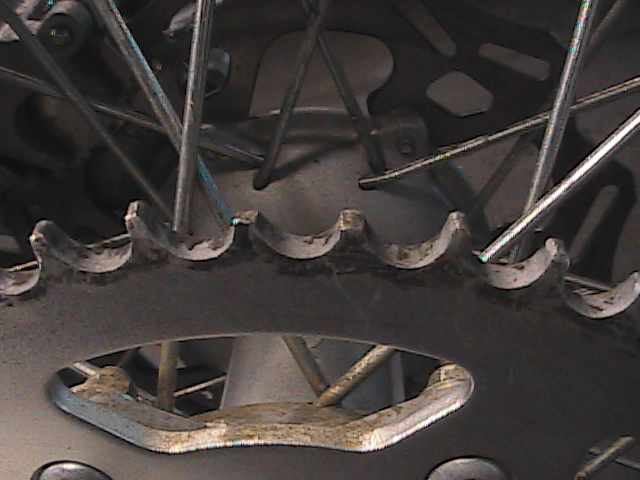Motorcycle rear sprocket with spokes visible, showing wear on teeth