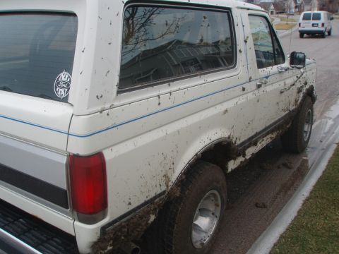 1987 Ford Bronco - This white 1987 Ford Bronco is heavily covered in mud, suggesting it has been driven off-road.