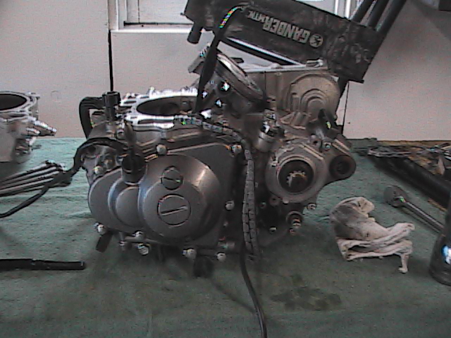 Motorcycle engine on a table with tools nearby. Text on a black part reads 'GANDERMTK'