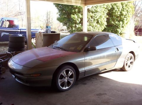 1995 Ford Probe - A 1995 Ford Probe with a contrasting red hood sits under a carport, with a blue pickup truck visible in the background.