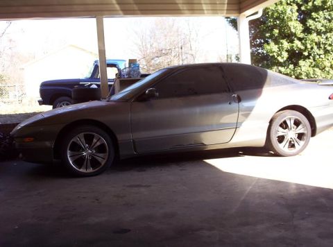 1995 Ford Probe - Side view of a 1995 Ford Probe coupe parked under a carport, with a blue pickup truck visible in the background.