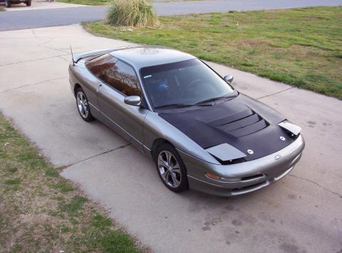 1995 Ford Probe - A silver Ford Probe is parked on a concrete driveway, a black hood with vents and pop-up headlights.
