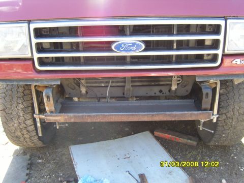 1989 Ford Bronco - Front view of a red Ford truck with a custom bumper modification, showing the grille and tires.