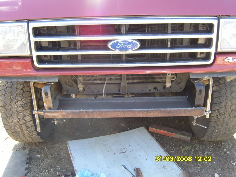 Red Ford truck front end, custom metal bumper installed, tires visible