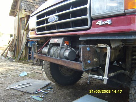 1989 Ford Bronco - Low front view of a dark red Ford truck with a Warn winch mounted behind a bare steel bumper bar, its cable spooled on the drum and a red b…