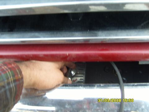 1989 Ford Bronco - A hand is shown working on a component behind the front grille of a vehicle.