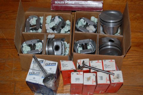 1994 Ford Bronco - Several sets of engine pistons and valves are laid out in cardboard boxes on a wooden surface.
