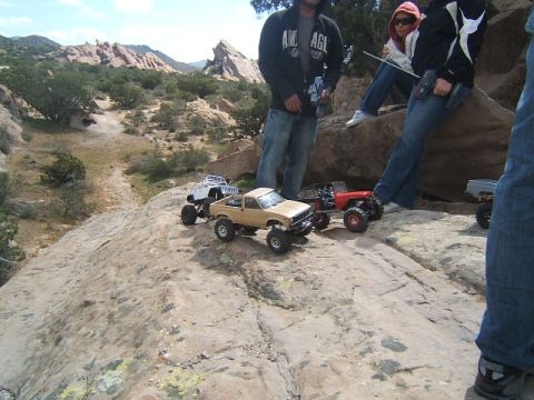 1988 Ford Bronco - Several radio-controlled trucks are positioned on a rocky terrain, with people observing them.