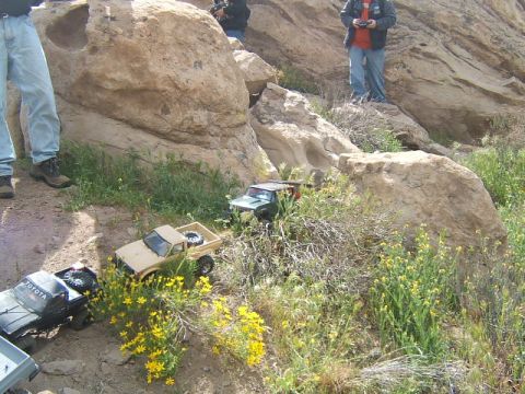1988 Ford Bronco - Remote control trucks are shown navigating a rocky, outdoor course with spectators present.