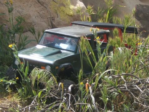 1988 Ford Bronco - A green Ford Bronco navigates a rocky, grassy terrain.