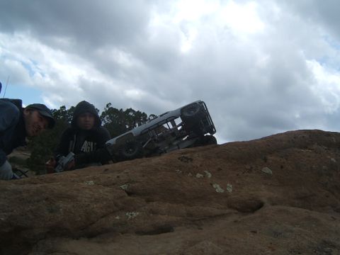 1988 Ford Bronco - Two individuals observe a remote control rock crawler navigating a rocky terrain under a cloudy sky.