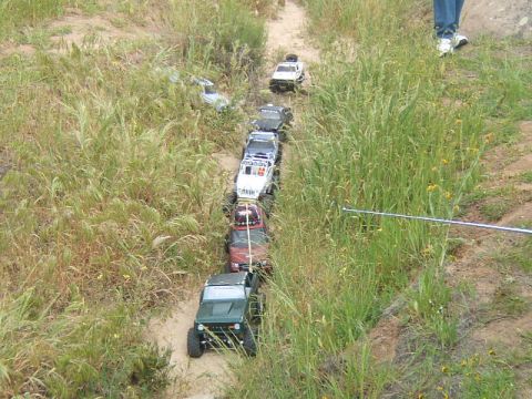 1988 Ford Bronco - A line of RC crawlers navigate a grassy, dirt trail during an outdoor event.