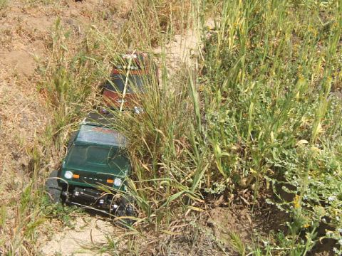 1988 Ford Bronco - Two remote control vehicles are partially hidden in dry grass and dirt.