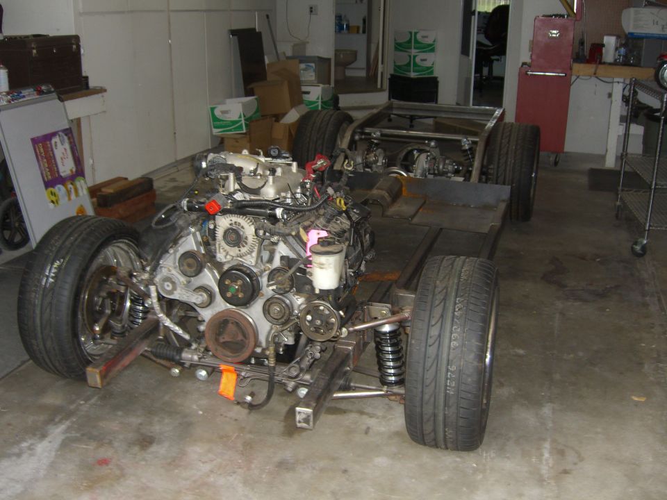 Bare car chassis with mounted V-engine and coil-over suspension in a garage build