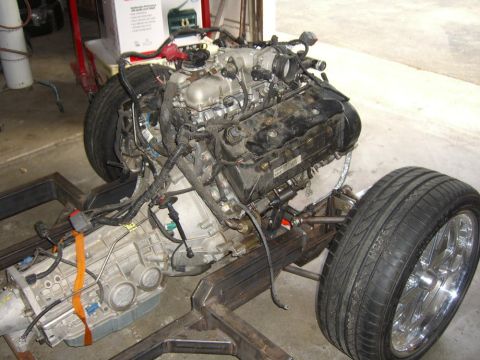 1964 Ford Ranchero - Engine and transmission assembly mounted on a custom frame with front suspension and chrome wheels visible.