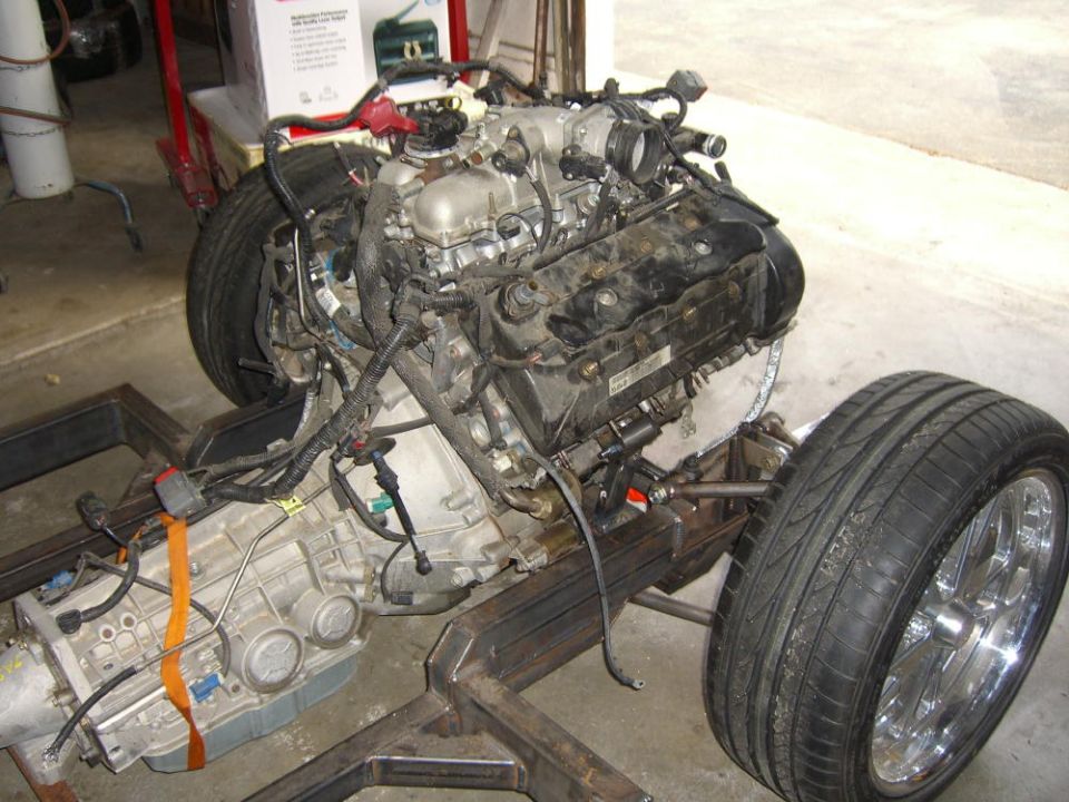V8 engine and transmission on a bare frame with a chrome wheel, in a garage build