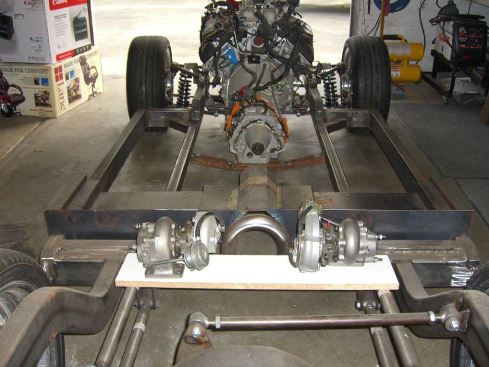Bare-steel custom chassis with V8 engine and twin turbos staged on the frame in a garage