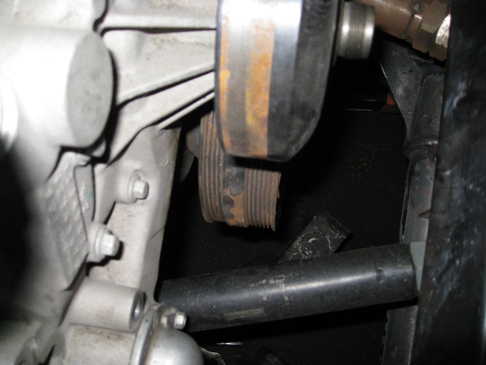 close-up of engine pulley with rust and a black pipe below
