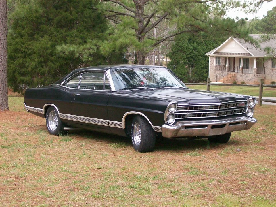 Black Ford Galaxie fastback coupe, front three-quarter view, chrome grille and white-letter tires, on a lawn