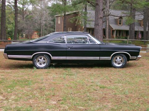 1967 Ford Galaxie - A black 1967 Ford Galaxie coupe is parked on a grassy lawn in front of a house.