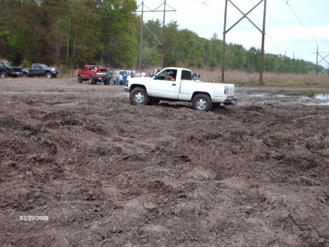 1982 Ford F-100 - Several trucks are seen off-roading in a muddy field on a cloudy day.
