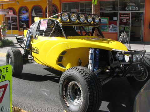 1990 Ford Bronco - yellow tube-chassis off-road buggy with a roof-mounted light bar and large BFGoodrich tires parked on a city street.