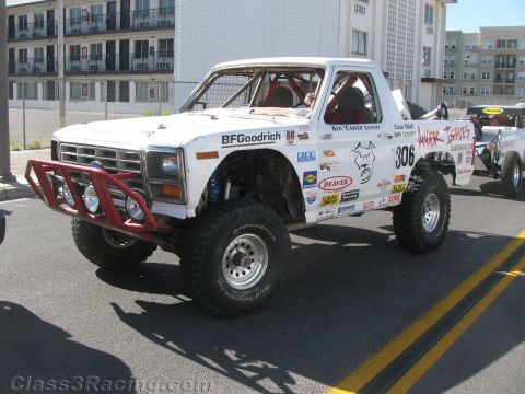 1990 Ford Bronco - white race-prepped pickup truck wearing number 306 and a red tube bumper, sponsor decals and off-road tires on a street.