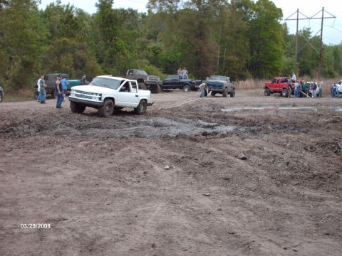 1982 Ford F-100 - Several trucks are gathered in a muddy area, with one white pickup truck appearing to be stuck.
