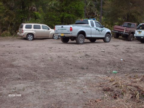 1982 Ford F-100 - A silver Ford F-150 pickup truck with law enforcement decals is parked next to other vehicles on a dirt lot.