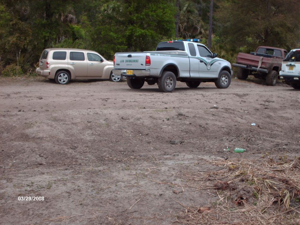 Silver Ford F-150 pickup truck, law enforcement markings, 3/4 front view, parked on dirt lot