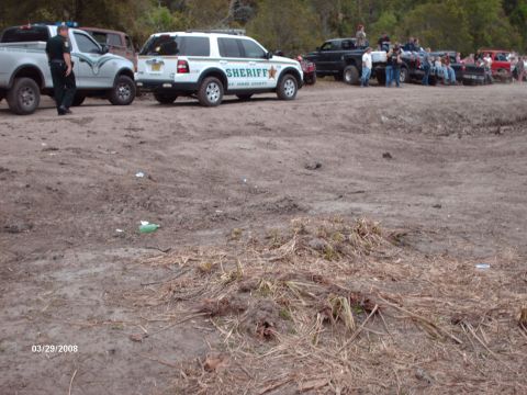1982 Ford F-100 - Multiple pickup trucks and a Sheriff SUV are parked on a dirt lot, with several people standing around.