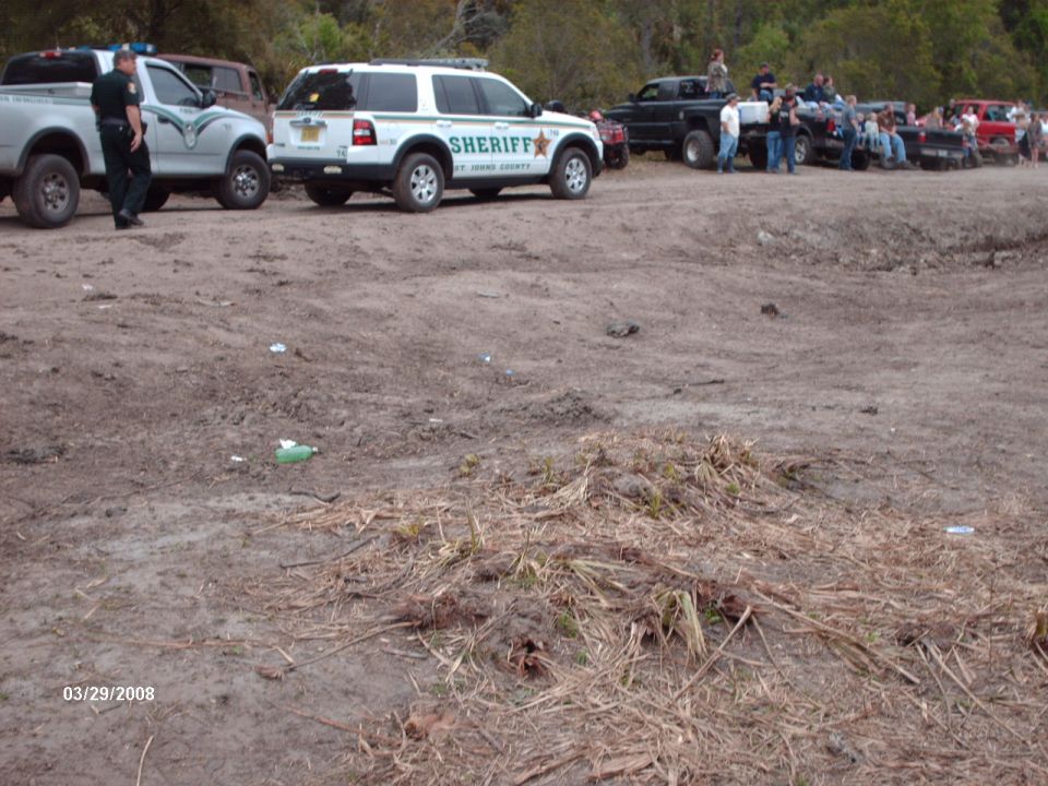 Sheriff SUV and pickup trucks parked on dirt with people gathered
