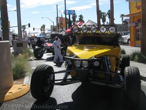 1990 Ford Bronco - yellow tube-chassis off-road buggy with a roof light bar staged on a street with a crew member and palm trees nearby.