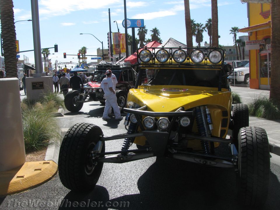 Yellow tube-chassis buggy with roof light bar staged on a street, people nearby