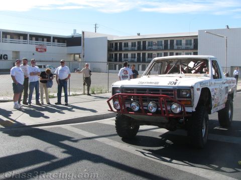 1990 Ford Bronco - white off-road race truck wearing number 306 sits on a street as a group of onlookers watches from the curb.