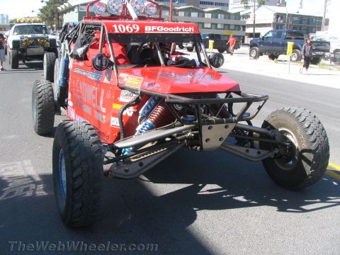1990 Ford Bronco - red tube-chassis off-road buggy wearing number 1069 with a roof light bar and blue coilover shocks staged on a street.
