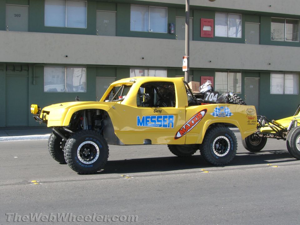 Yellow off-road truck lettered MESSER and MAXXIS parked by a building