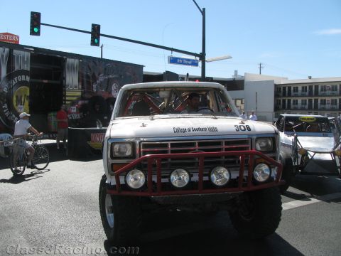 1990 Ford Bronco - white lifted off-road truck numbered 306 and lettered College of Southern Idaho faces forward at a street event with a green traffic light…