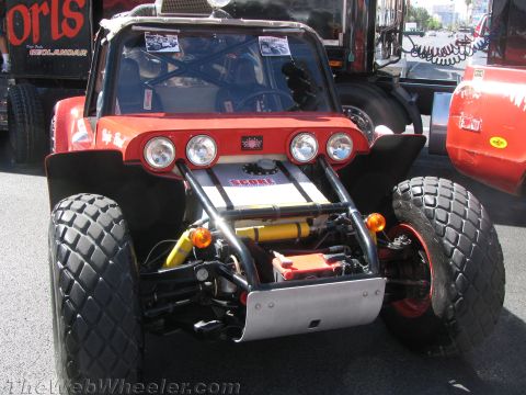 1990 Ford Bronco - red and black tube-frame off-road buggy shows its front end with four round lights and large knobby tires at a street display.