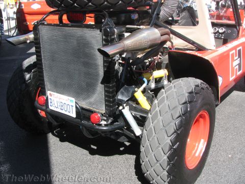 1990 Ford Bronco - rear of an orange off-road buggy reveals its radiator, plumbing and Borla exhaust above a license plate reading BAJABOOT.