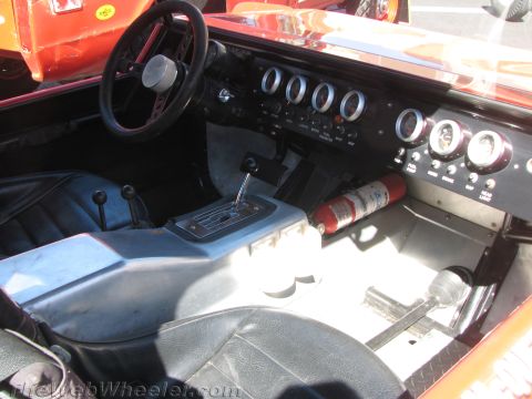 1990 Ford Bronco - cockpit of an off-road buggy shows its steering wheel, row of round gauges, automatic shifter and a mounted fire extinguisher.