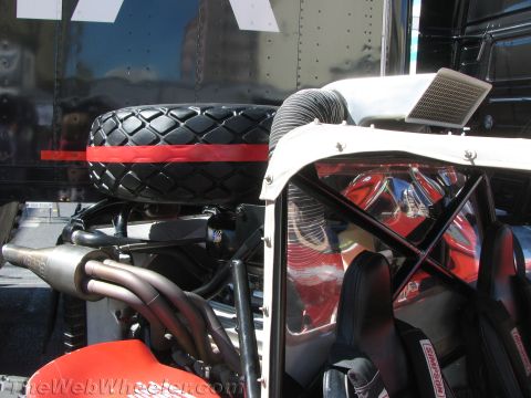 1990 Ford Bronco - spare tire with a red stripe sits above the engine, exhaust and red roll-cage cockpit of an off-road race buggy.