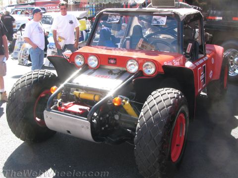 1990 Ford Bronco - red and black tube-frame off-road buggy with four front lights sits at a street event as people stand around it.
