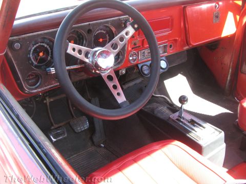 1990 Ford Bronco - vintage truck cockpit shows a chrome three-spoke steering wheel, round gauges, floor shifter and a red-and-white bench seat.