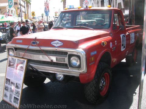 1990 Ford Bronco - red vintage Chevrolet race pickup numbered 40 with roof lights sits on display beside an informational placard at a crowded street show.